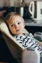 Portrait of a cute blonde toddler. Beautiful baby boy sitting in a high chair waiting, looking away. He is sad