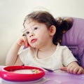 Portrait of cute bored Caucasian child kid girl sitting in high chair eating cereal with spoon early morning Royalty Free Stock Photo