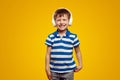 Portrait of cute boy in headphones listening to music and smiling isolated over yellow background Royalty Free Stock Photo