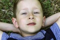 Portrait of cute boy lying back on the grass with his hands behind his head. Boy is showing his tongue. Close up Royalty Free Stock Photo