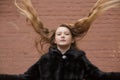 Portrait of cute brunette teen girl in black fur coat on the background of brown brick wall . Cosiness, fashion, style Royalty Free Stock Photo