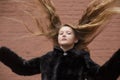 Portrait of cute brunette teen girl in black fur coat on the background of brown brick wall . Cosiness, fashion, style Royalty Free Stock Photo