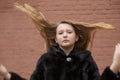 Portrait of cute brunette teen girl in black fur coat on the background of brown brick wall . Cosiness, fashion, style Royalty Free Stock Photo