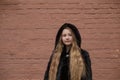 Portrait of cute brunette teen girl in black fur coat on the background of brown brick wall . Cosiness, fashion, style Royalty Free Stock Photo