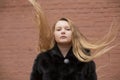 Portrait of cute brunette teen girl in black fur coat on the background of brown brick wall . Cosiness, fashion, style Royalty Free Stock Photo