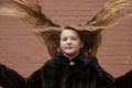 Portrait of cute brunette teen girl in black fur coat on the background of brown brick wall . Cosiness, fashion, style Royalty Free Stock Photo