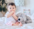 Portrait of cute caucasian baby girl playing with soft fluffy toy on bed in bedroom. Little adorable infant girl sucking Royalty Free Stock Photo