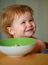 Portrait of cute Caucasian child kid with spoon. Hungry messy baby with plate after eating puree.