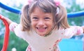 Portrait of cute Caucasian litte girl wearing white dress with flowers hanging on monkey bars on a summer day. Girl Royalty Free Stock Photo