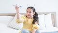 Portrait of cute Caucasian little girl with pony tails hair sitting on bed at home and playing with airplane model toy, holding Royalty Free Stock Photo