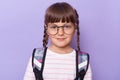 Portrait of cute charming schoolgirl in glasses wearing backpack standing looking at camera with smile, with calm facial