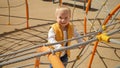 Portrait of cute cheerful baby boy climbing up on the rope ladder at playground. Children playing outdoor, kids outside, summer Royalty Free Stock Photo