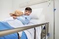 Portrait of cute child alone in hospital room lying in bed with teddy bear looking at camera with copy space