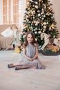 Cute child girl sitting against Christmas tree indoors. Royalty Free Stock Photo