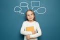 Portrait of cute child girl with speech clouds bubbles holding yellow book on blue blackboard. Royalty Free Stock Photo