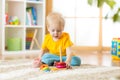 Portrait of cute child toddler boy assembling colorful pyramid toy on floor at living room