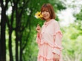 Portrait of a cute Chinese girl in pink dress holding wild flower and smiling at camera in summer forest. Outdoor fashion portrait Royalty Free Stock Photo