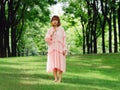 Portrait of a cute Chinese girl in pink dress holding wild flower and smiling at camera in summer forest. Outdoor fashion portrait Royalty Free Stock Photo