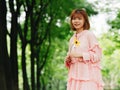 Portrait of a cute Chinese girl in pink dress holding wild flower and smiling at camera in summer forest. Outdoor fashion portrait Royalty Free Stock Photo