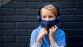 Portrait cute cool blonde caucasian little young boy in casual blue hoodie and medical protective mask stands city Royalty Free Stock Photo