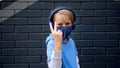 Portrait cute cool blonde caucasian little young boy in casual blue hoodie and medical protective mask stands city
