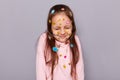 Portrait of cute dreaming little brown haired little girl covered with stickers posing isolated over gray background, looks shy,