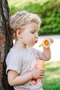 Portrait of cute funny little blond Caucasian child girl toddler standing in the green forest field meadow blowing soap bubbles Royalty Free Stock Photo