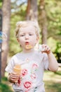 Portrait of cute funny little blond Caucasian child girl toddler standing in the green forest field meadow blowing soap bubbles Royalty Free Stock Photo