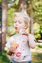 Portrait of cute funny little blond Caucasian child girl toddler standing in the green forest field meadow blowing soap bubbles Royalty Free Stock Photo