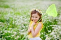 Portrait of a cute girl with a flower wreath on her head standing in a field of daisies with a butterfly net