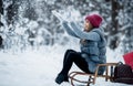 Portrait of a cute girl in a gray fur coat and red hat holds sled and walking in a winter forest in a snowy day. Winter mood. Royalty Free Stock Photo