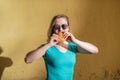 Portrait of a cute girl in a green dress walking outside and eating a burger on a warm summer day. Beautiful blonde in sunglasses