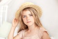 Portrait of a cute girl in a straw hat. Thoughtful little blonde with long hair sits on the bed in a bright children`s room. Child