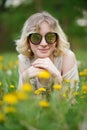 portrait of a cute girl in sunglasses, girl smiles, girl lies resting in the grass on the lawn with dandelion flowers Royalty Free Stock Photo