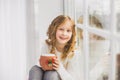 Portrait of cute happy little girl sitting on windowsill Royalty Free Stock Photo