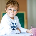 Portrait of cute happy school kid boy with glasses at home making homework. Little child writing with colorful pencils Royalty Free Stock Photo