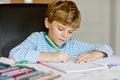 Portrait of cute healthy happy school kid boy at home making homework. Little child writing with colorful pencils Royalty Free Stock Photo