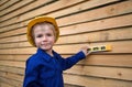 Portrait of cute inquisitive boy 6 years old in blue overalls and in construction helmet with level tool in hands