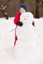 Portrait of cute kid boy in red winter clothes making big snowman in the park on a sunny cold day. Child having fun outdoors. Royalty Free Stock Photo