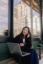 Portrait of cute Korean girl in cafe near window and networking, looking at laptop and drinking coffee. Student having cappuccino Royalty Free Stock Photo