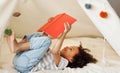 Cute little african american kid curly boy reading book in play tent Royalty Free Stock Photo