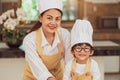 Portrait cute little Asian boy chef with eyeglasses and his mother looking to camera in home cooking kitchen happily and funny. Royalty Free Stock Photo