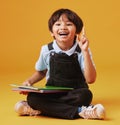 Portrait of a cute little asian boy sitting on the floor while reading against an orange background. Happy and content Royalty Free Stock Photo