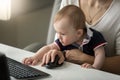 Portrait of cute little baby boy sitting on mothers lap and reaching for computer keyboard Royalty Free Stock Photo