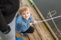 Portrait of cute little blond boy sitting on wooden pier near father. Adorable child having fun and smiling at lake or river shore Royalty Free Stock Photo