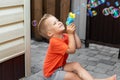 Portrait of cute little blond kid boy enjoy having fun play blowing soap bubbles siiting at home yard outdoors on bright Royalty Free Stock Photo