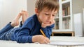 Portrait of cute little boy doing homework on carpet in living room. Concept of domestic education and child development Royalty Free Stock Photo