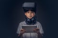 Portrait of a cute little boy dressed in a white t-shirt, with virtual reality glasses and headphones is holding a Royalty Free Stock Photo