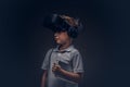 Portrait of a cute little boy dressed in a white t-shirt, with virtual reality glasses and headphones is holding a Royalty Free Stock Photo