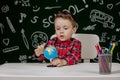 Portrait of cute little boy holding in hands small globe on blackboard background. Ready for school. Back to school